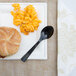 A black WNA Comet EcoSense plastic spoon on a plate with a sandwich and macaroni and cheese.