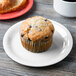 A muffin on a white GET Diamond White narrow rim plate next to a cup of coffee on a table in a breakfast diner.