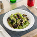 A Dart white foam plate with salad, blackberries, and cheese on it with a plastic fork.