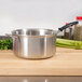 A Vollrath stainless steel sauce pan with a black handle on a wooden surface.