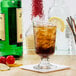 A Libbey footed highball glass filled with a drink and ice on a counter.