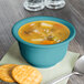 A Fiesta turquoise China bouillon bowl filled with soup with a spoon and crackers on a napkin.