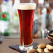 A close up of a glass of Anchor Hocking beer with a few peanuts on a table.