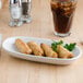 A Tuxton eggshell china relish tray with fried egg rolls and a drink on a table.