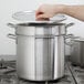 A hand opening a large silver pot with a lid.