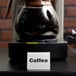 A Tablecraft stainless steel tent sign that says "Coffee" on a table with a coffee machine.