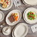 An Acopa ivory scalloped oval stoneware platter with meat and vegetables on a wood surface.