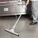 A person using a Unger SmartFit floor squeegee with a telescoping handle to clean a kitchen floor.