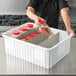 A person pouring brown liquid from a plastic bottle into a white Metro tote box.