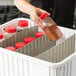 A person pouring brown powder into a white Metro tote box with a red lid.