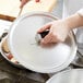 A hand holding a Torogard handle on a Vollrath aluminum pan lid over a pan with a spatula inside.