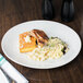 A Tuxton bright white china platter with a chicken breast and macaroni on a table.