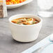 An Acopa ivory stoneware bouillon cup with a spoon on a table.