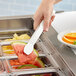 A hand using Cambro white plastic tongs to serve a slice of watermelon.