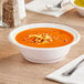 A white Dart plastic bowl filled with soup on a table with a spoon.