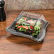 A salad in a black Fineline plastic bowl on a table.