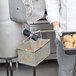 A person in a white chef's uniform holding a metal basket of potatoes.