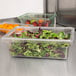 A Carlisle clear plastic food storage box with greens in it.