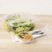 A clear plastic Genpak deli container of salad with a high dome lid and a fork.