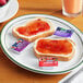 A plate of bread with grape, strawberry, and mixed fruit jelly on it.