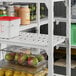 A white Cambro Camshelving® Premium vented shelf with containers of green apples, green grapes, and a jar of fruit.