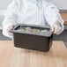 A chef holding a black Cambro food pan filled with food.