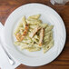 A close up of a Tuxton Sonoma bright white china plate with pasta, chicken, and sauce.