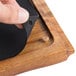 A hand placing a black silicone pad onto a Tablecraft Acacia Wood Underliner.