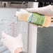 A person in gloves pouring Noble Chemical Arctic Ice Machine Cleaner from a container into a measuring cup.