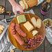 A Tablecraft acacia wood display platter of cheese and grapes.