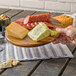 A hand holding a Tablecraft acacia wood display board with cheese and meat.