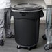 A man standing next to a Rubbermaid black commercial trash can.