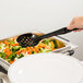 A person using a black Cambro perforated salad bar spoon to serve vegetables.