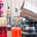 A person pours red liquid into a Waring commercial bar blender.