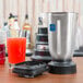 A Waring commercial bar blender on a counter next to a glass of red liquid.