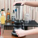 A person using a Waring commercial bar blender on a table in a cocktail bar.