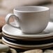 A stack of Libbey Driftstone sand satin matte porcelain coupe plates on a table with a white cup.