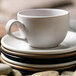 A white cup on a stack of Libbey Driftwood Satin Matte Porcelain saucers.