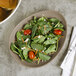 A Libbey sand satin matte organic porcelain coupe plate with a salad of spinach, tomatoes, and feta.