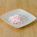 A white bowl filled with Rokz peppermint cocktail rimming sugar with red crystals on top.