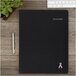 An At-A-Glance black planner with pink ribbon on it.