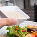 A person holding a white square Elite Global Solutions melamine bowl filled with food.