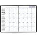 A spiral bound black At-A-Glance monthly planner with white pages featuring numbers and letters.