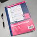 An Adams 3-part carbonless rent receipt book with blue and pink covers and a pen holder with a pen inside.