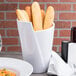 A white container with food inside sitting on a table with bread.