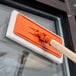 A 3M Doodlebug orange pad holder with a wooden handle on a window.