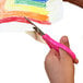 A child's hand uses Westcott stainless steel pointed tip scissors to cut a rainbow drawing.