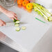 A person cutting cucumber on a WebstaurantStore flexible cutting board.