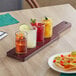 An Acopa mahogany flight paddle with Straight Up Tasting Glasses on a table with a glass of liquid with a lime wedge.