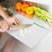 A person cutting cucumbers on a WebstaurantStore flexible cutting board.